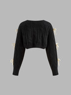 Black cropped cable knit cardigan with long sleeves and cream bow-knots accenting the sides.
