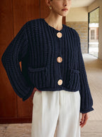 Chunky navy blue knit cardigan with large gold buttons, styled with white high-waisted trousers.