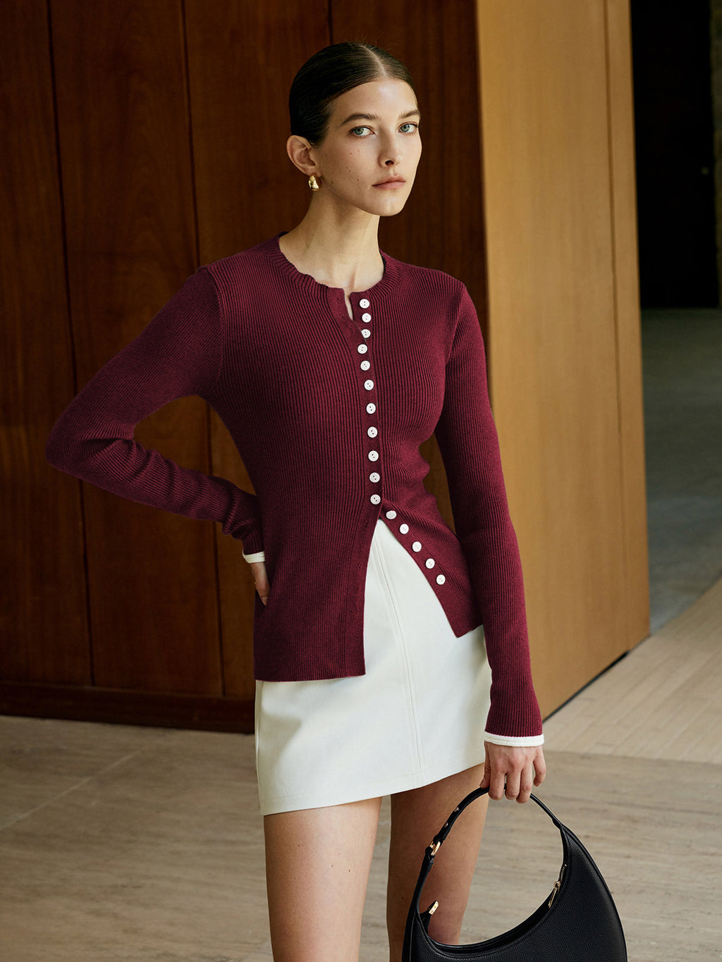A burgundy classic knitted cardigan with button closure, paired with a white mini skirt.