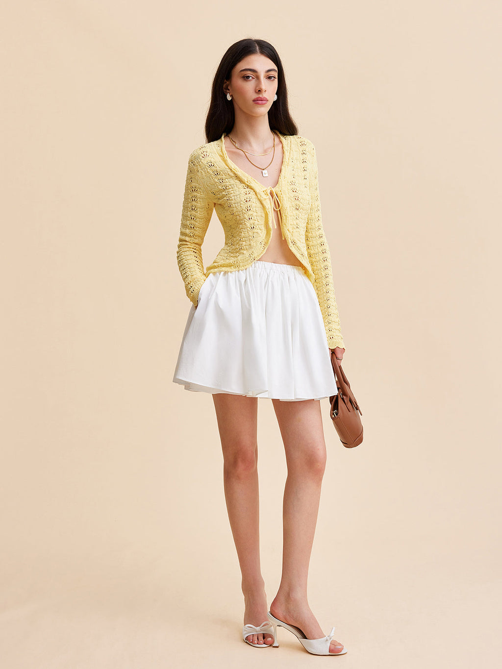 A crocheted cardigan sweater with a tie-front design, paired with a white skirt and sandals.