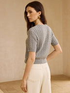 A cable knit short-sleeve cardigan sweater paired with cream high-waisted pants.